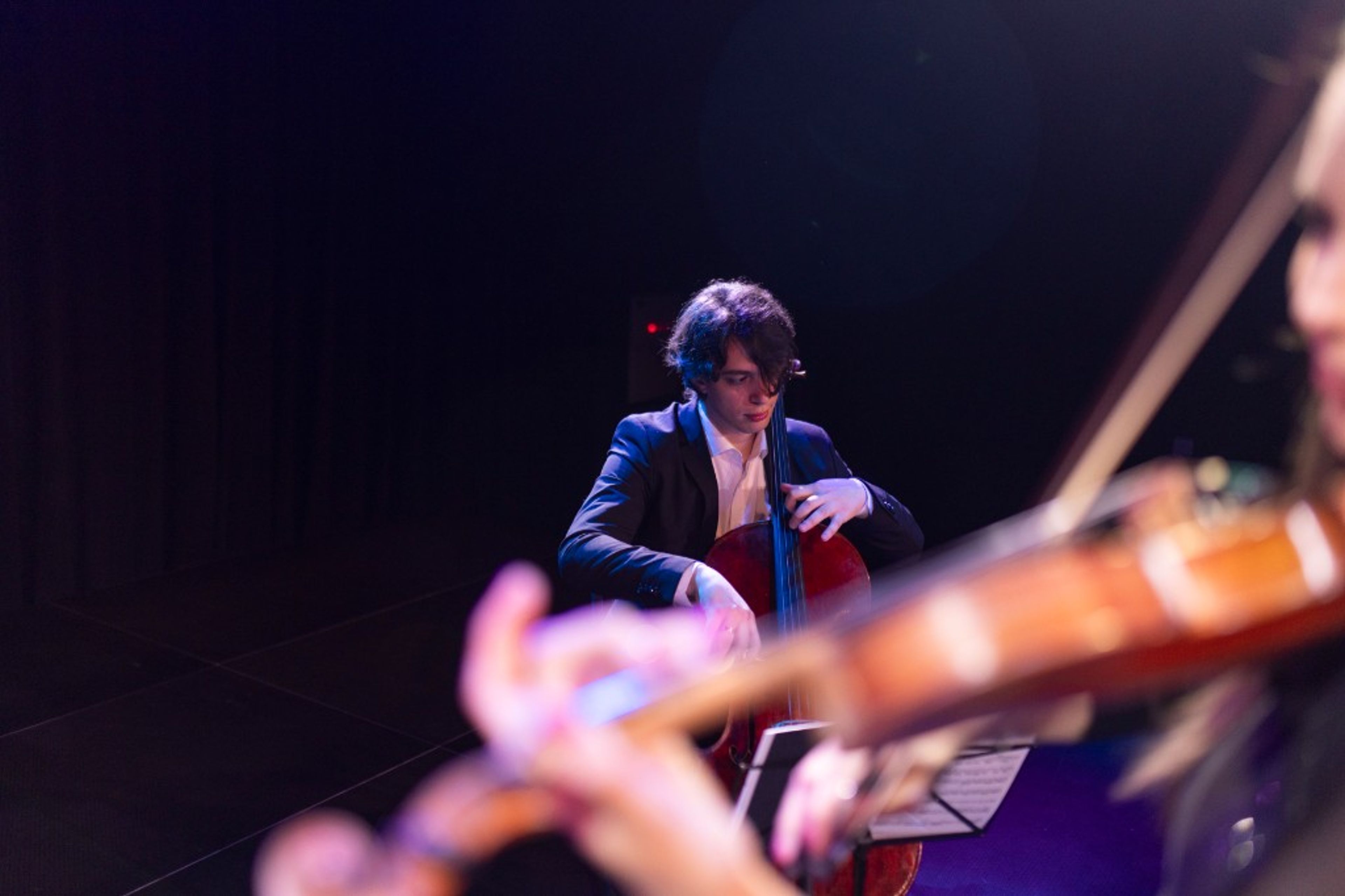 A musician performing with a cello on a dark stage under a spotlight.