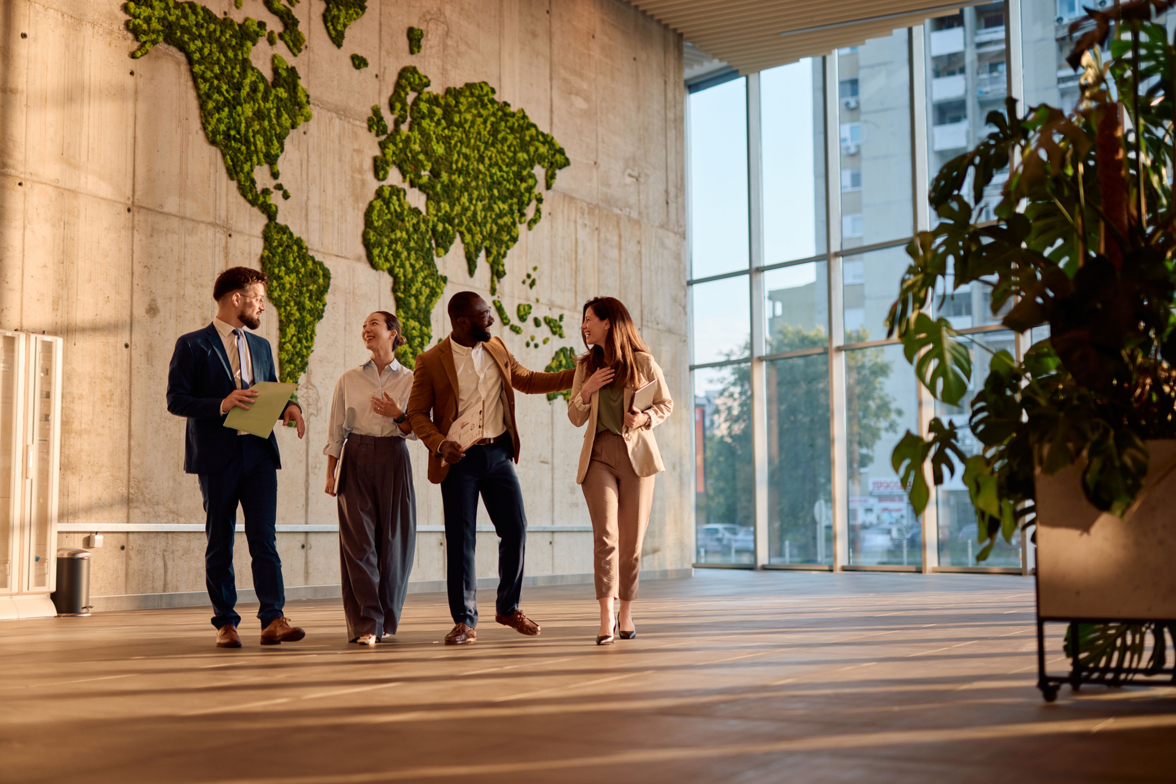 Business colleagues walking and talking in a modern office lobby with a living world map on the wall.