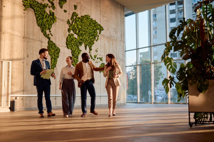 Business colleagues walking and talking in a modern office lobby with a living world map on the wall.