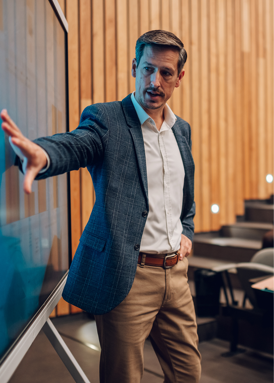 A professor presenting beside a screen in a lecture hall