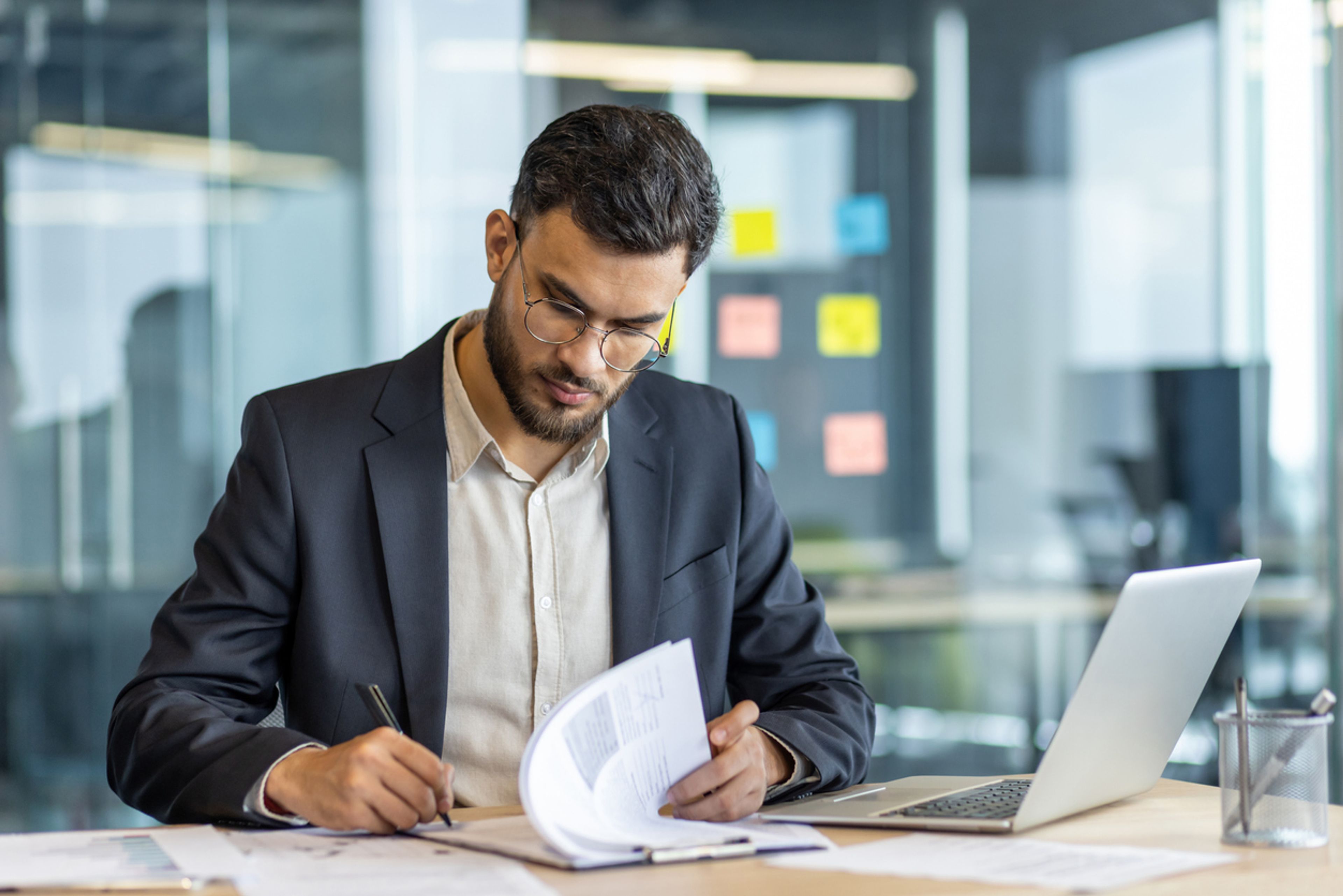 A business man sits at a desk signing paperwork.