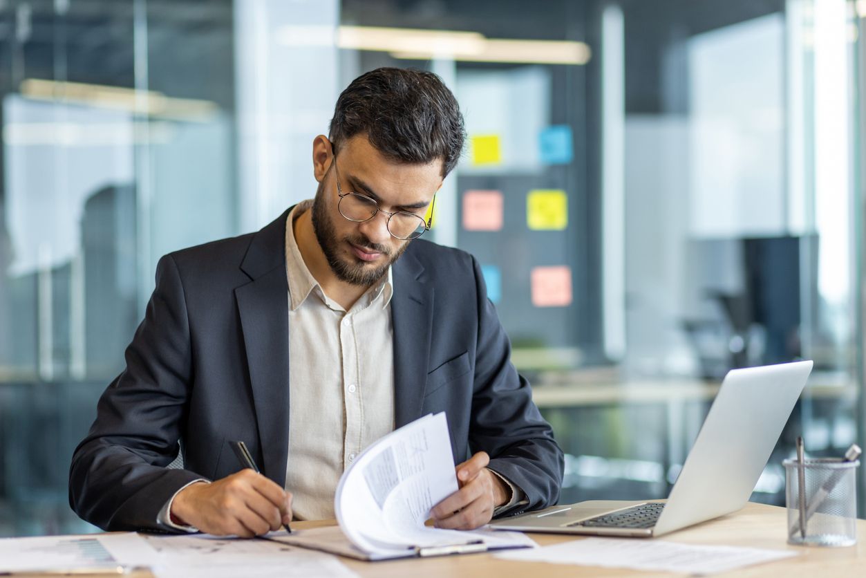 A business man sits at a desk signing paperwork.