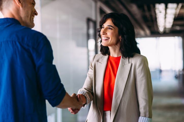 A middle-aged professional woman shakes hands with someone in an officespace.