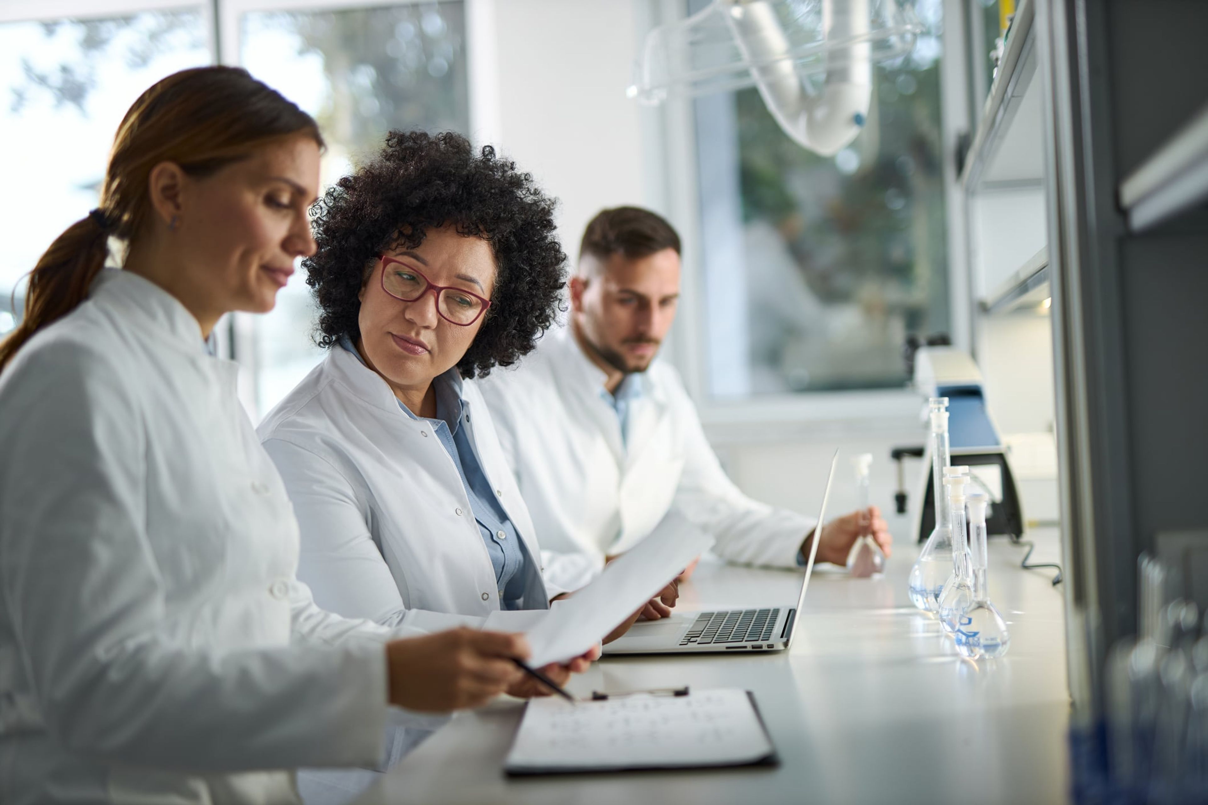 Scientists discussing work in front of a lab bench with a laptop and paper.