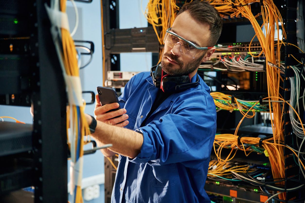 Young man is working with internet equipment and wires in server room.
