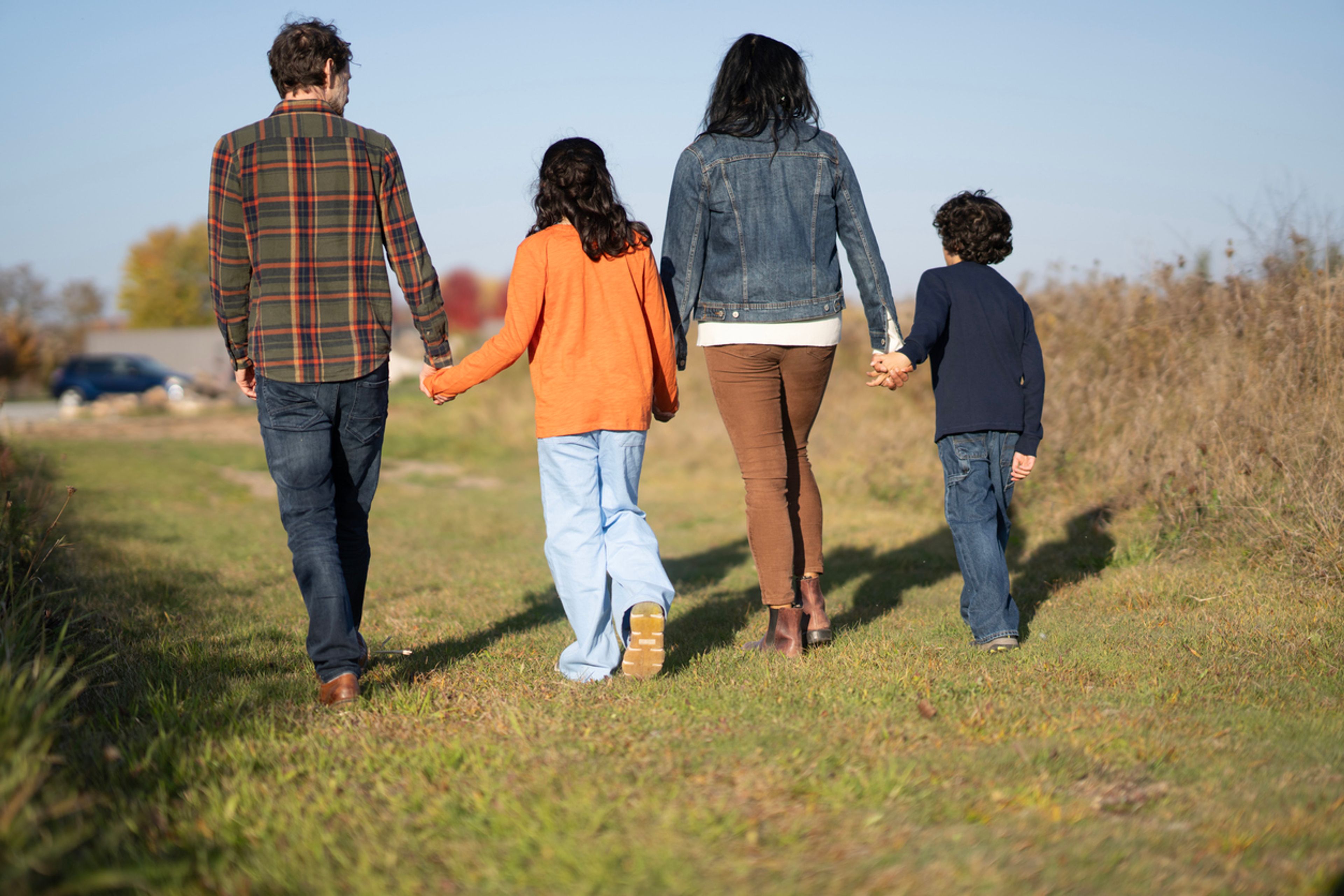 A family in a grass yard is walking hand-in-hand toward a house.