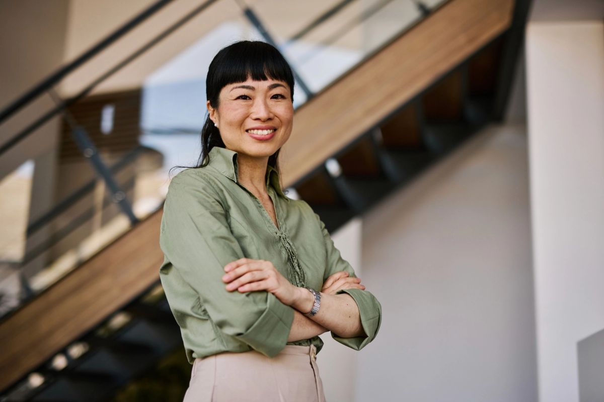Woman in a green shirt standing with her arms crossed in front of a staircase.