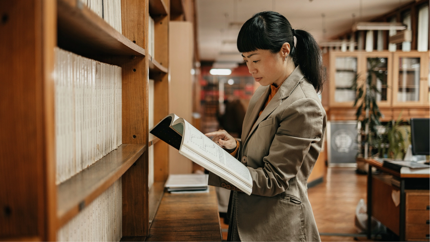 A researcher reviewing a journal in a library aisle