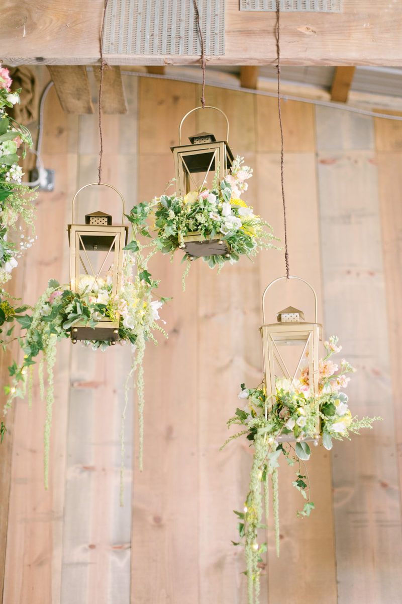 hanging gold lanterns filled with peach, yellow, and white flowers with green hanging amaranthus spilling out
