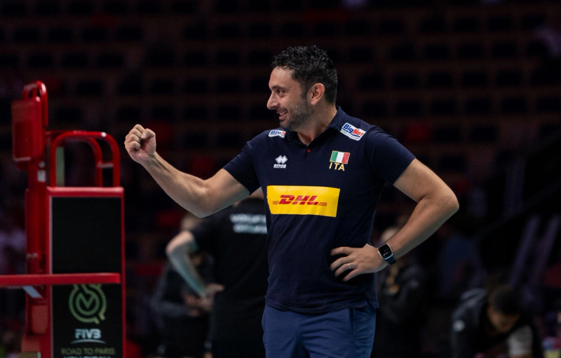 A man in a navy sports shirt with Italian flags and sponsor logos celebrates with a fist pump.