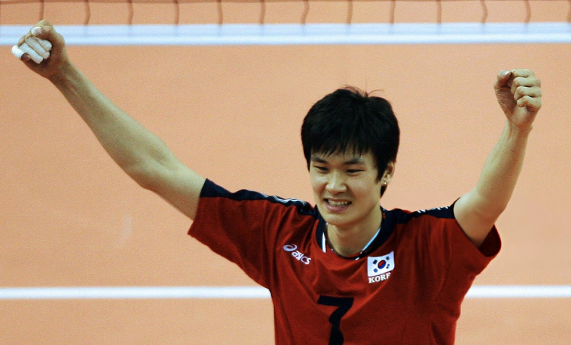 A volleyball player in a red jersey with the South Korean flag celebrates with both arms raised.