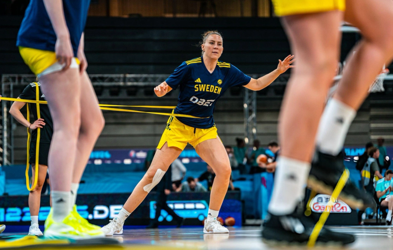 Athletes in yellow and blue uniforms engage in a resistance band training session on a basketball court.