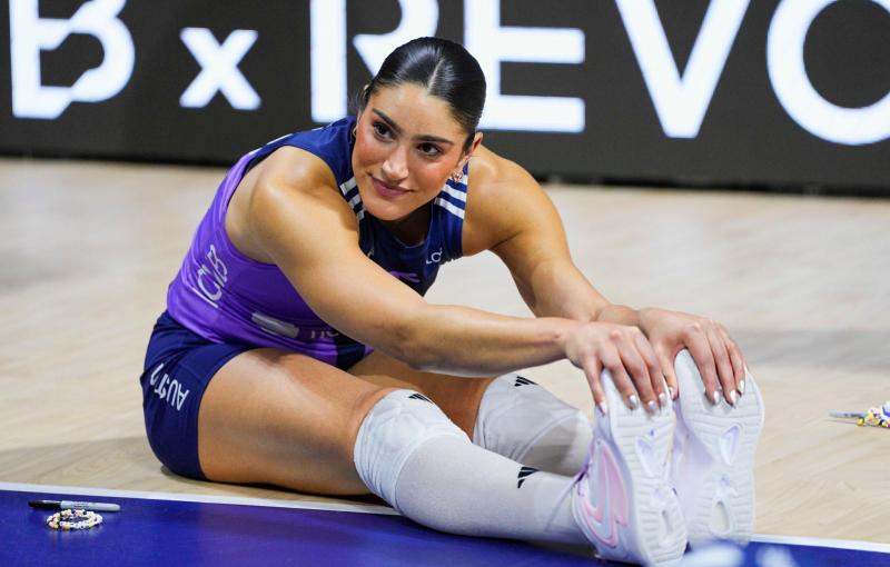 Athlete in a purple uniform stretching on the floor, reaching for their feet.