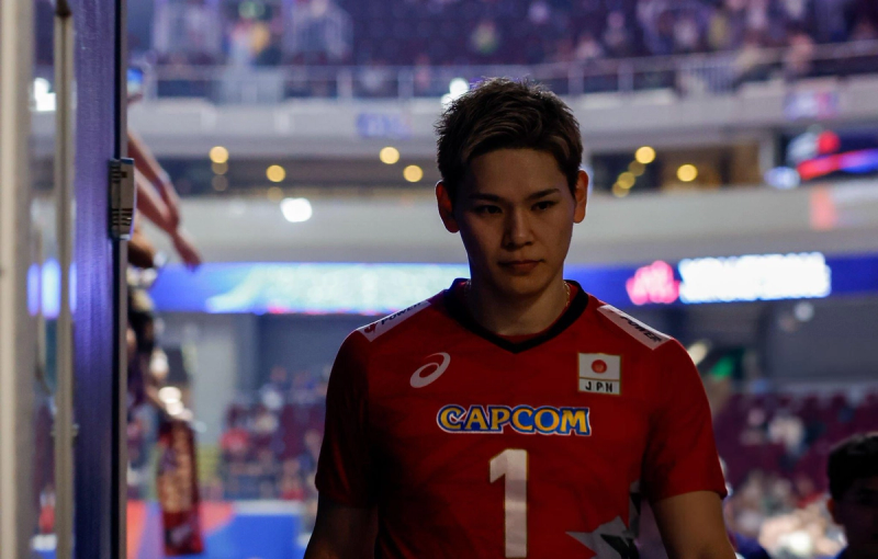 Volleyball player wearing a red jersey with the number 1 and "CAPCOM" logo, walking in a dimly lit sports arena.