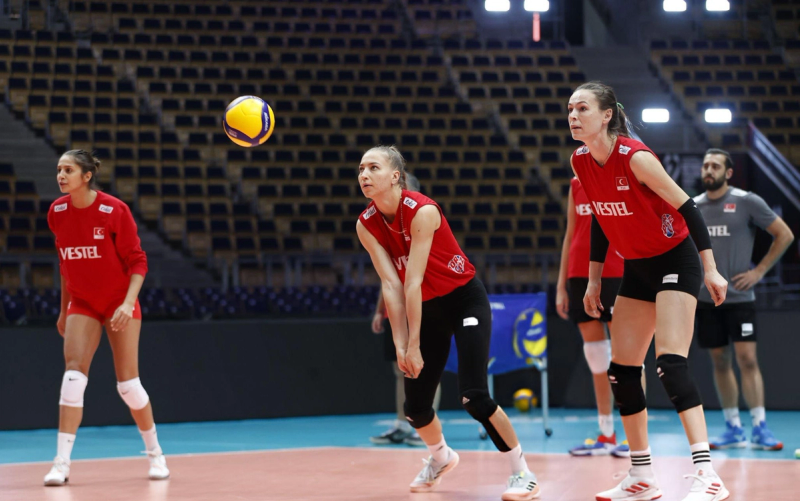 Volleyball players in red uniforms practicing on an indoor court, focusing on a yellow and blue ball in the air.