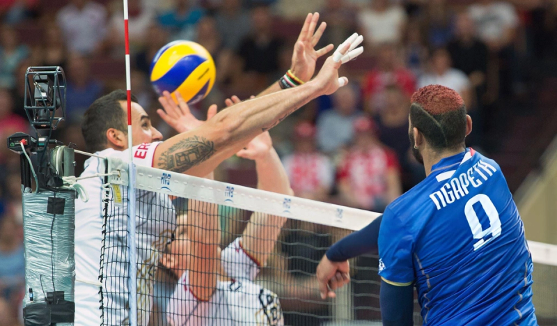 Two volleyball players attempt to block a spike from a player in a blue jersey during a match.