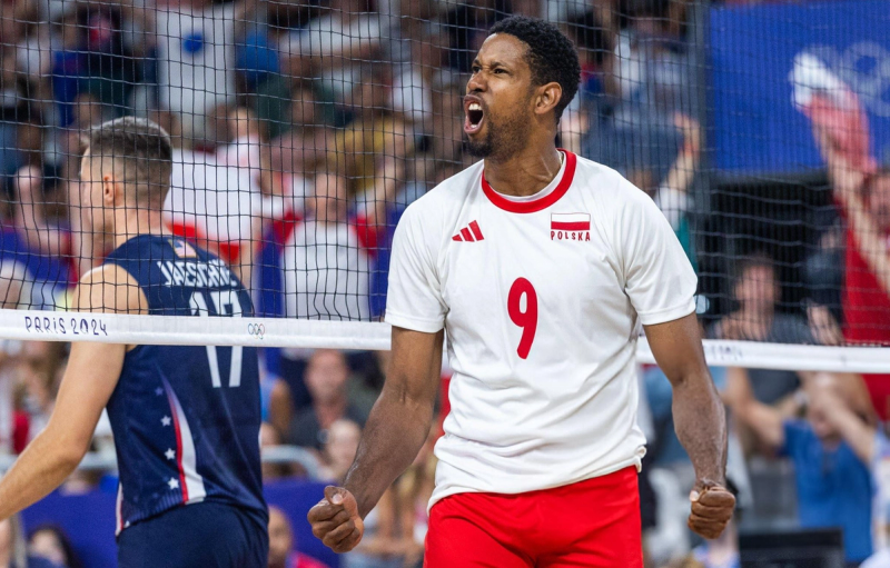 A volleyball player in a white and red uniform with the number 9 celebrates exuberantly on the court during a match. Another player is partially visible in the background.