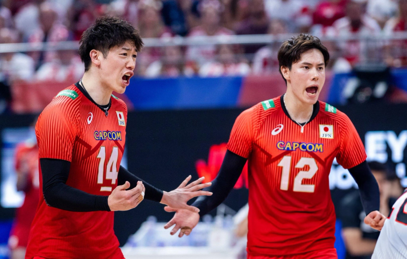 Two volleyball players in red jerseys with Japanese flags are expressing strong emotions on the court during a game.