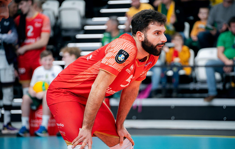 Volleyball player in red uniform leaning forward, focused during a game.
