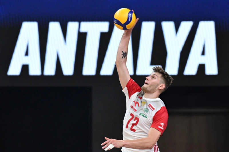 A volleyball player in a red and white uniform jumps to hit the ball with "ANTALYA" displayed on the screen behind.