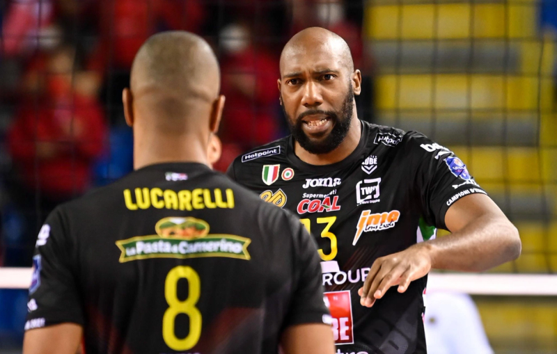 Two volleyball players in black jerseys engage in a focused discussion during a match. One player has "Lucarelli" written on their back.