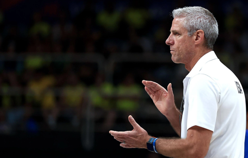 A man in a white shirt claps his hands, appearing focused, with a blurred crowd in the background.
