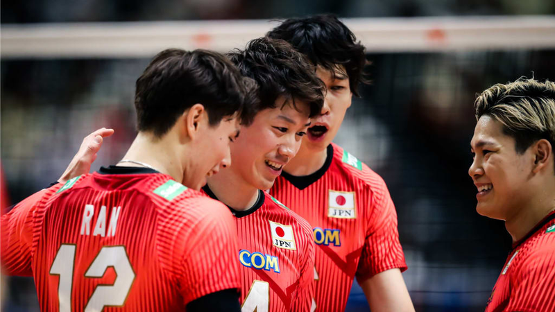 A group of volleyball players in red jerseys with Japan's flag, smiling and celebrating during a game.