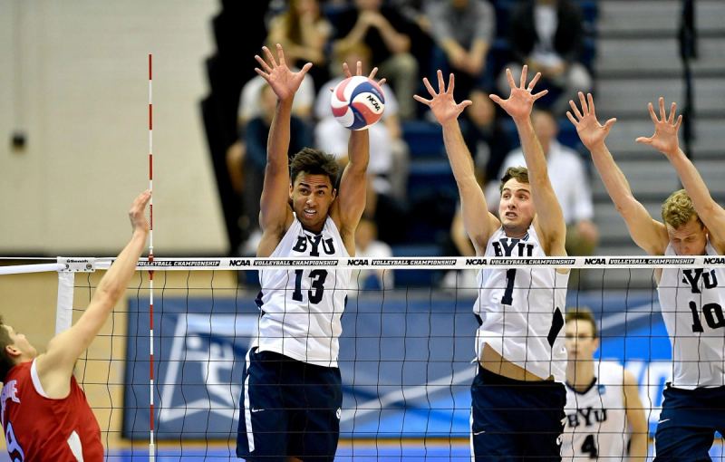 Three volleyball players from BYU jump to block a ball at the net during an NCAA Volleyball Championship match.