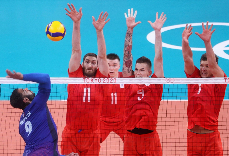 Volleyball player in blue spikes the ball against a team in red attempting to block at the Tokyo 2020 Olympics.