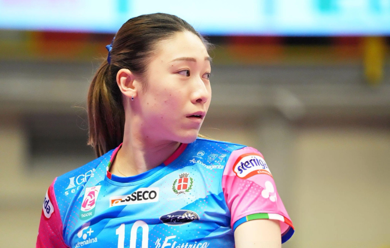 A volleyball player in a blue and pink jersey looks to the side, with various sponsor logos on the shirt.