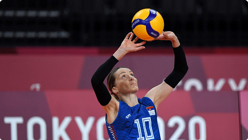 A volleyball player in a blue jersey with the number 10 is preparing to strike the ball during a match at the Tokyo 2020 Olympics.