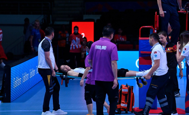 A volleyball player is being carried off the court on a stretcher by medical staff. Some officials and team members are standing nearby.