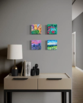 four small paintings above a small desk with a lamp and books