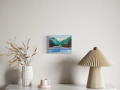 small blue painting of hills in blue and green over a table with a lamp and dried grasses