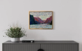 A painting of hills around a river hanging on a wall above a credenza with a flower arrangement