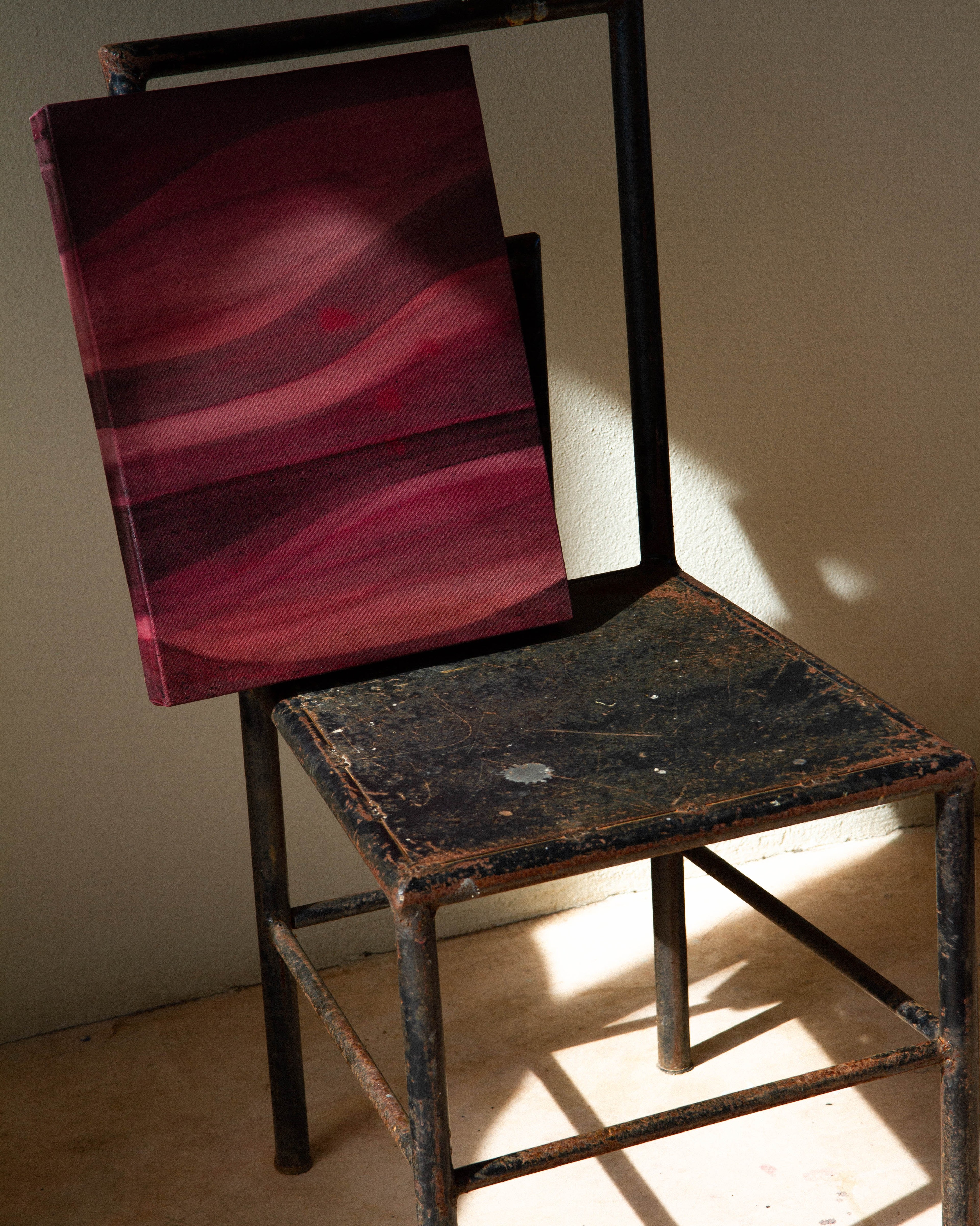 An abstract painting on canvas using layered earth pigments resting on a chair in the studio.