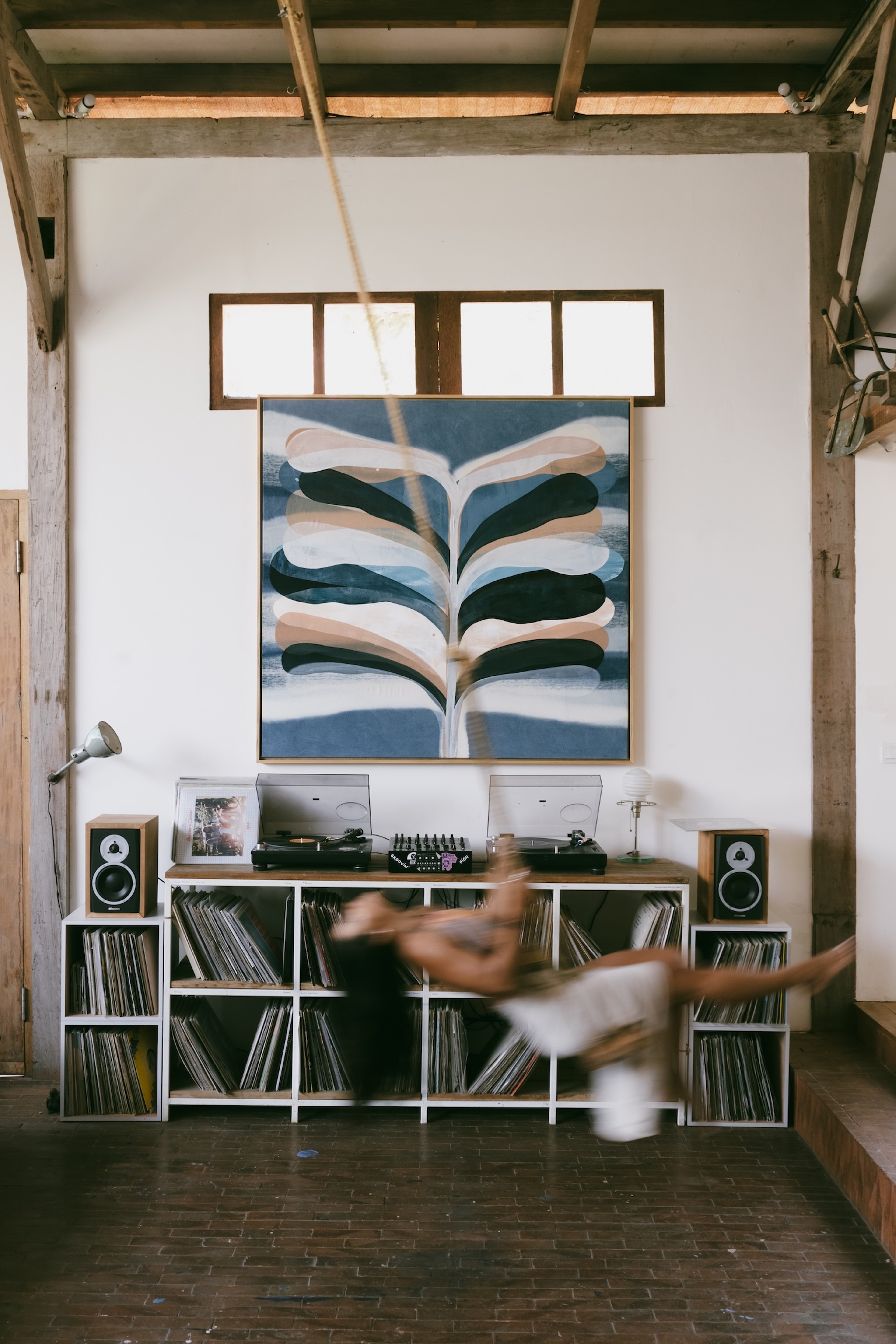 Indigo painting by Jake Paul White in a studio setting, with the artist standing near a record player and a woman swinging in front of the artwork