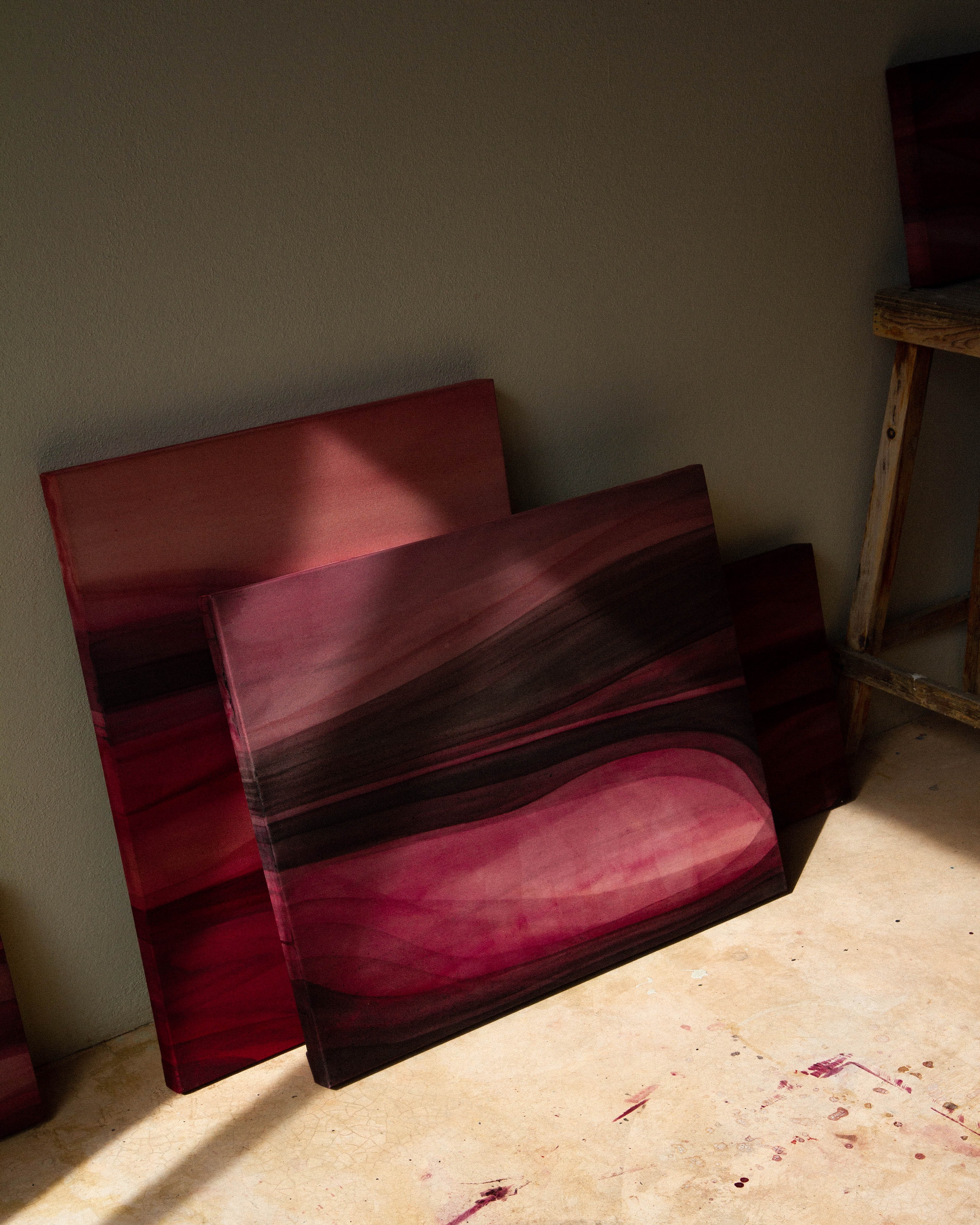 Abstract paintings stacked against a wall in warm natural light on the studio floor.
