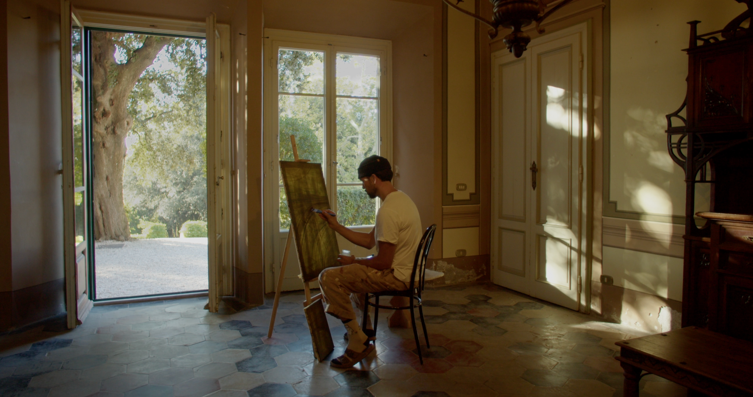 Jake Paul White painting at an easel inside the 19th-century villa at Villa Lena, with tall doors open onto the garden.