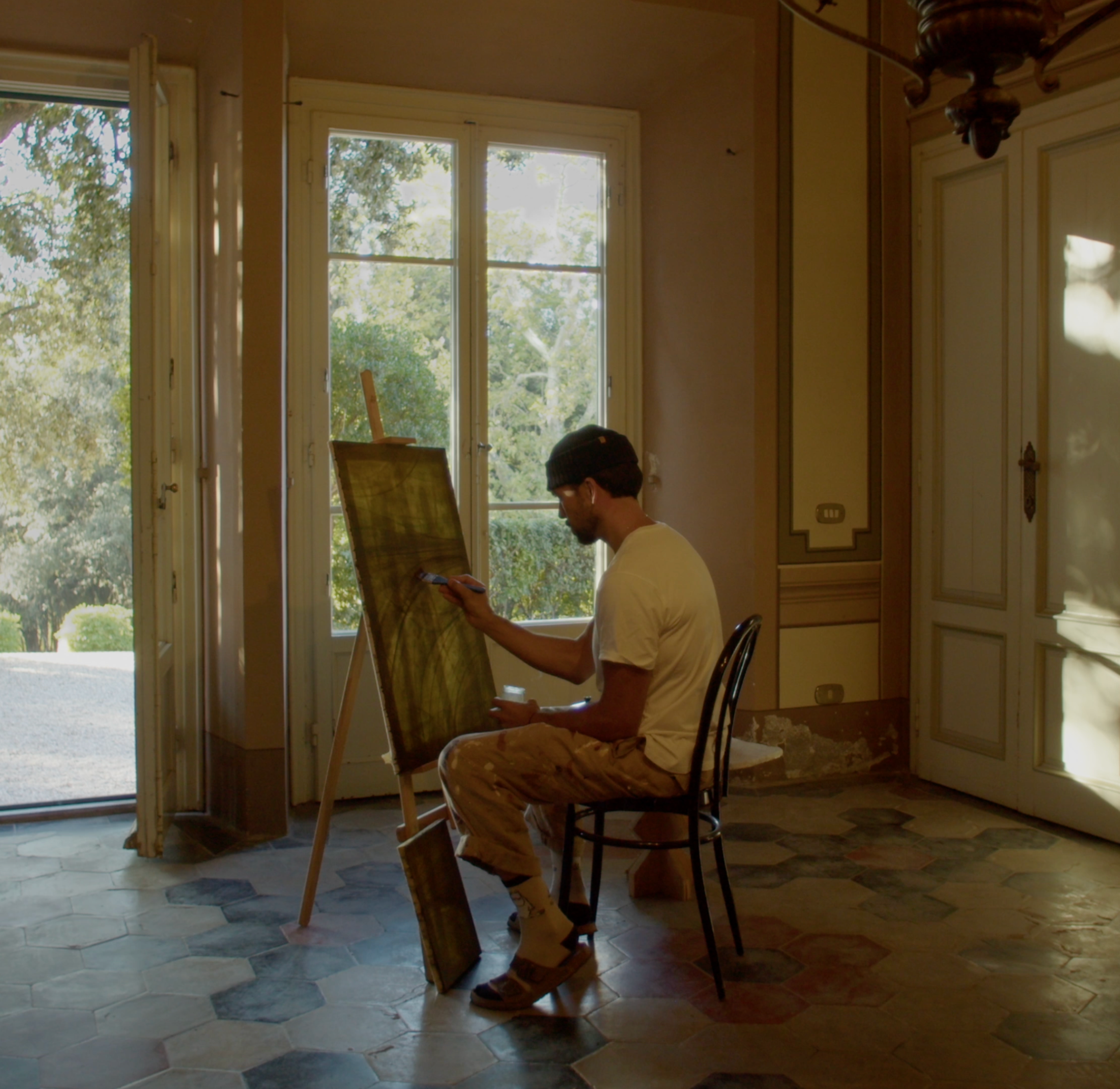 Jake Paul White painting at an easel inside the 19th-century villa at Villa Lena, with tall doors open onto the garden.