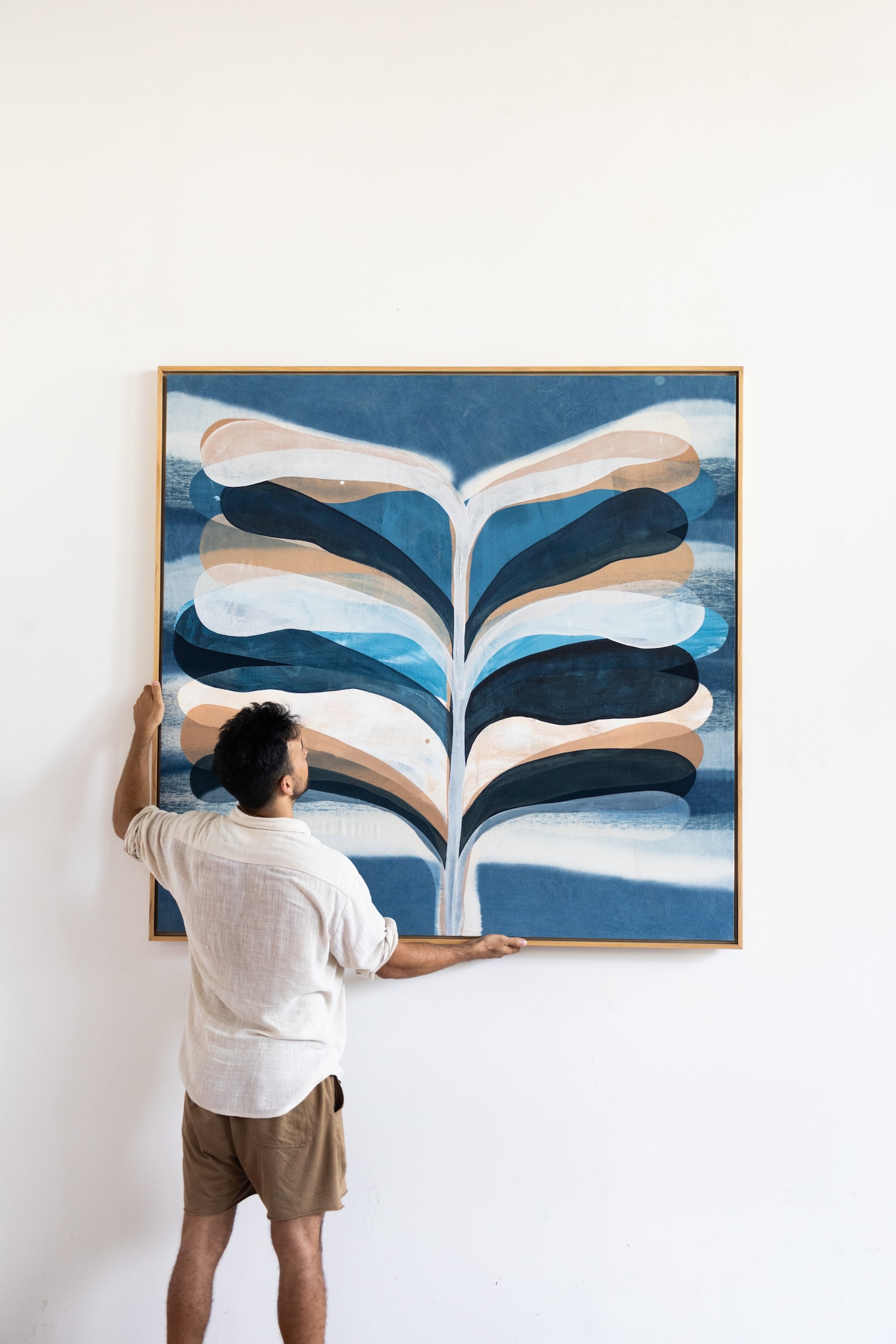 Jake Paul White installing an indigo painting on a gallery wall, captured mid-process with the artwork partially hung