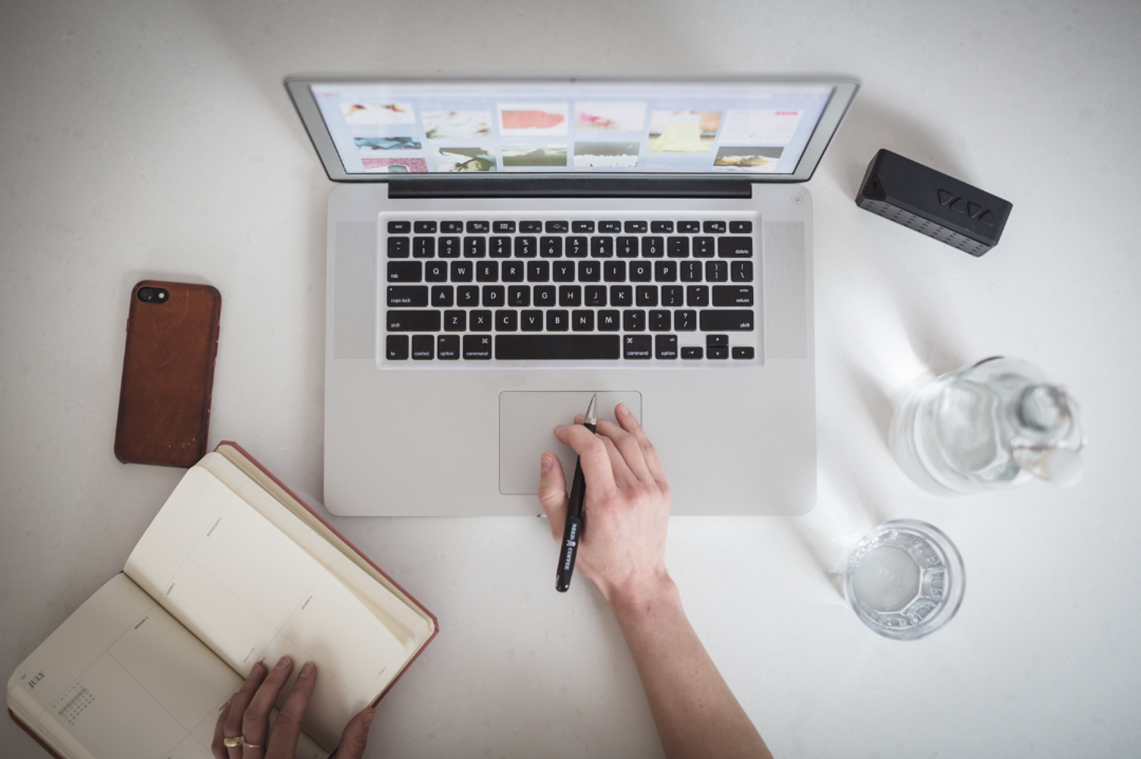 Person writing in a notebook sitting at a desk with a laptop