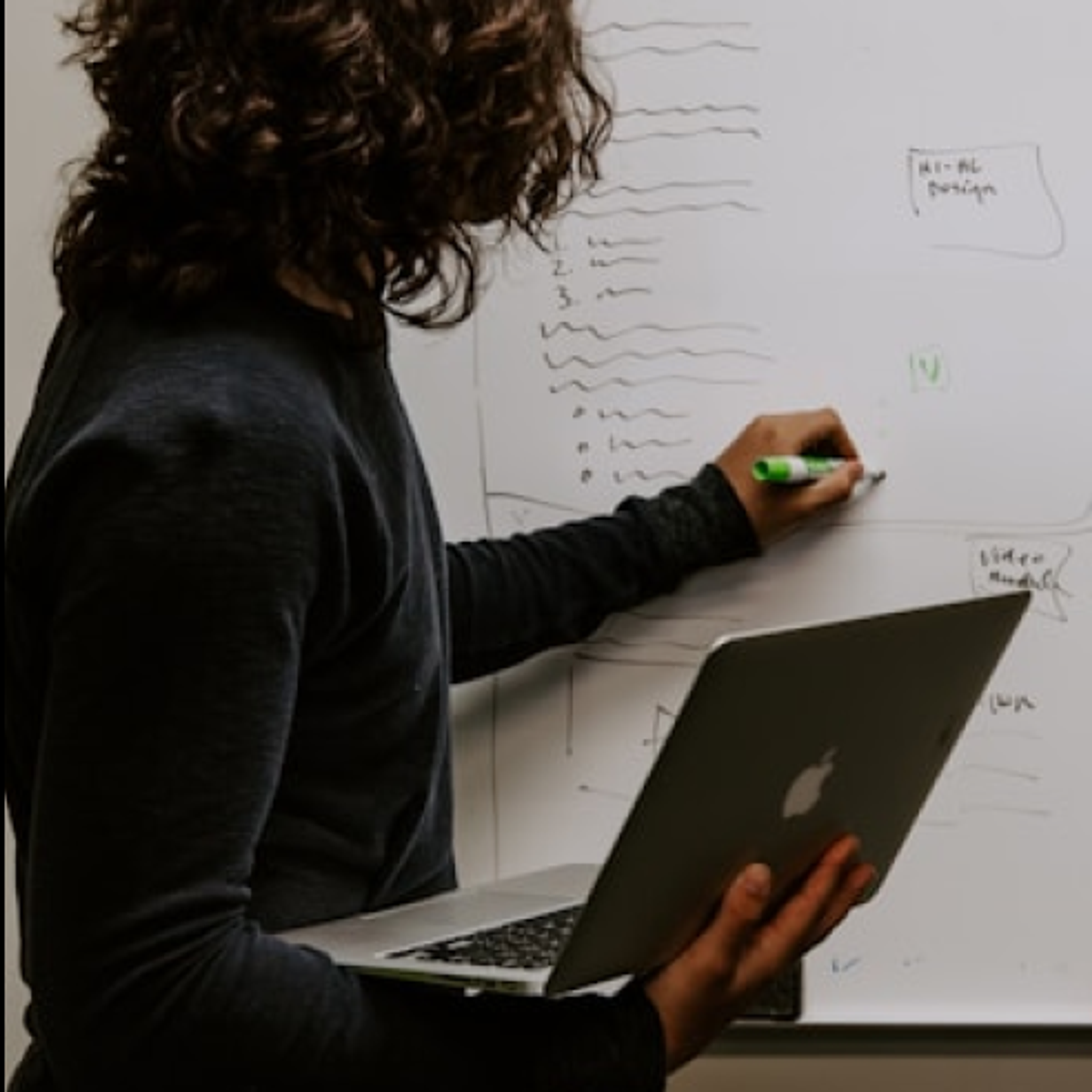 Woman writing on a whiteboard holding a MacBook