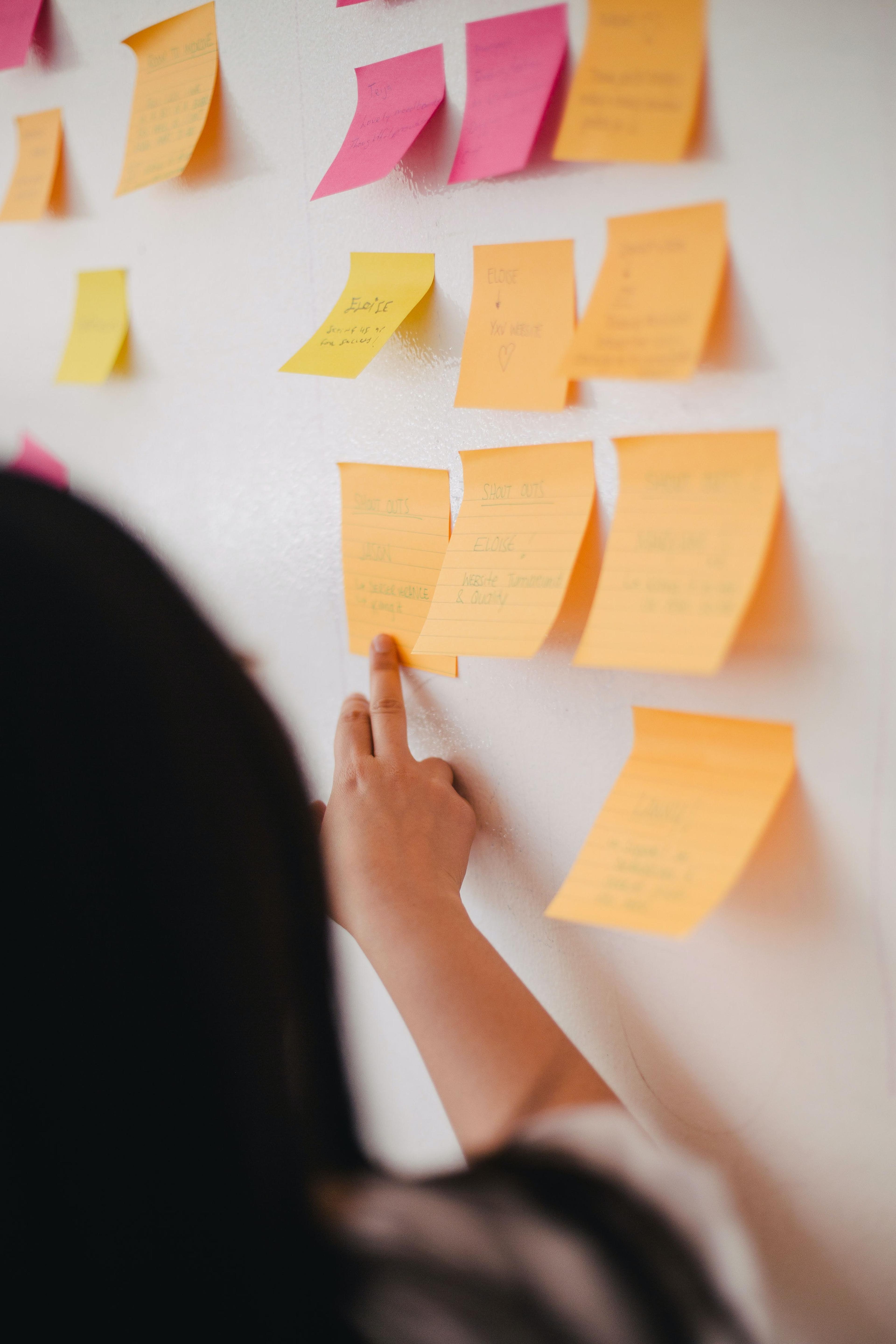 Person pointing at sticky notes on a plain white wall