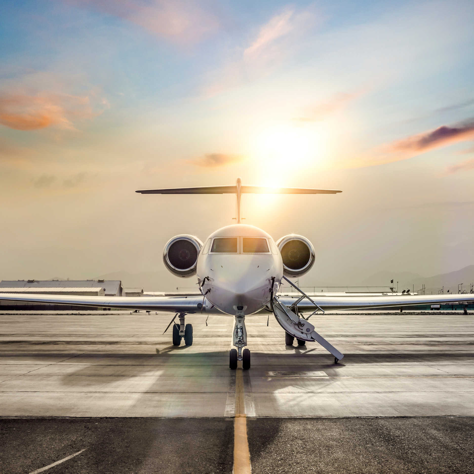 Private jet on a runway with boarding ladder dropped and sunshine in the background