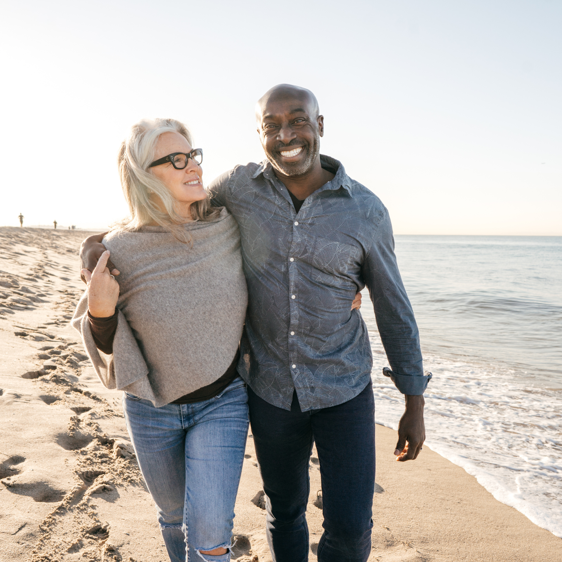 Two smiling people walking on a beach with an ocean background