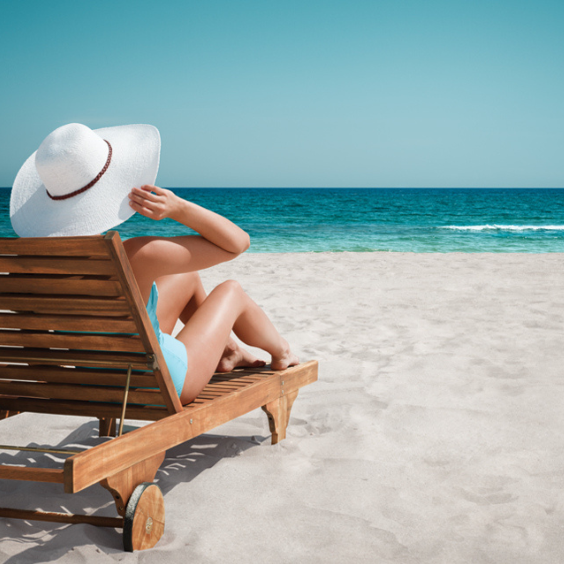 Woman sitting in a sun chair with a white hat on a white beach