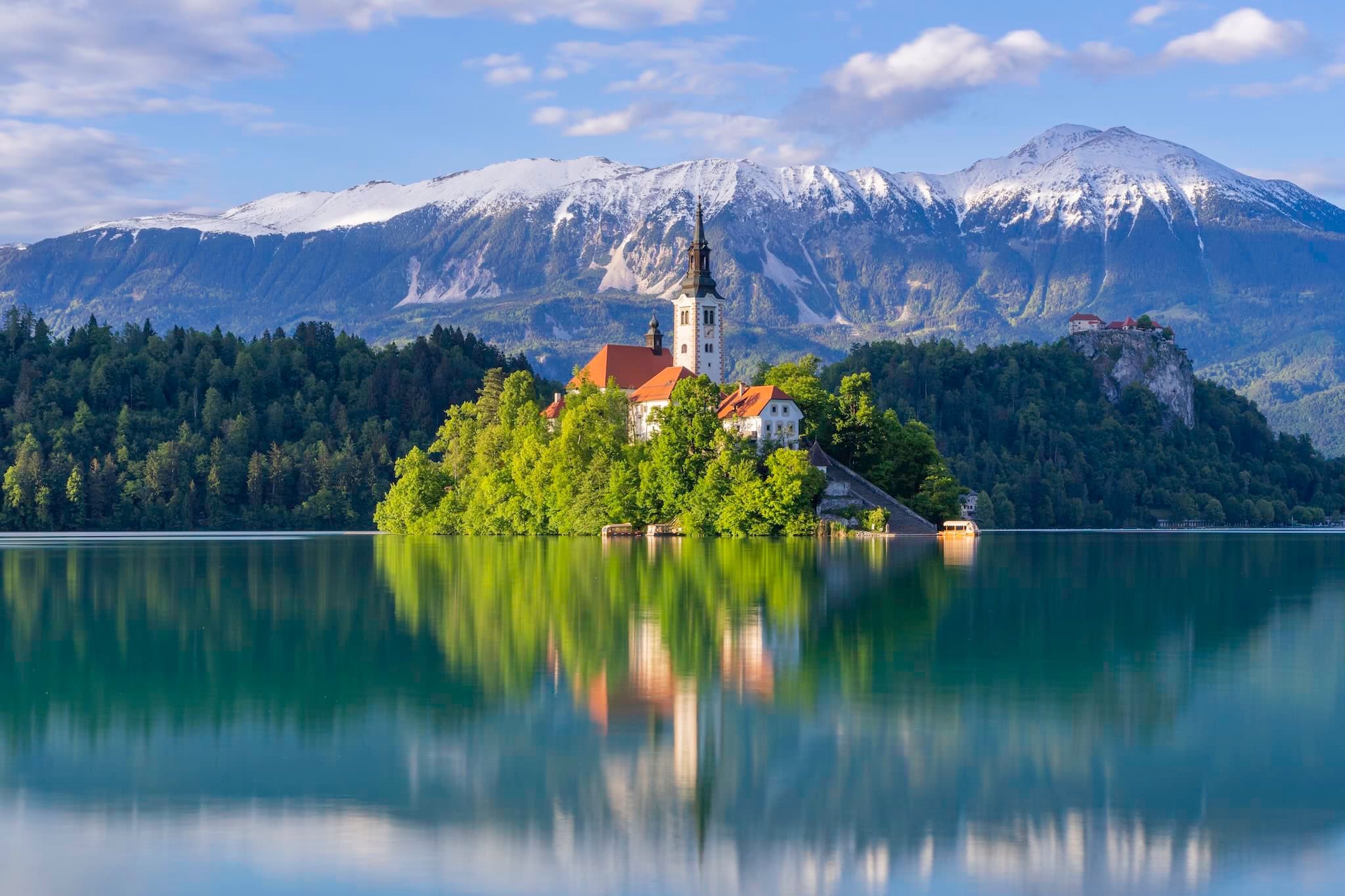 May: The church on Bled Island with snow-capped peaks behind it, Lake Bled, Slovenia