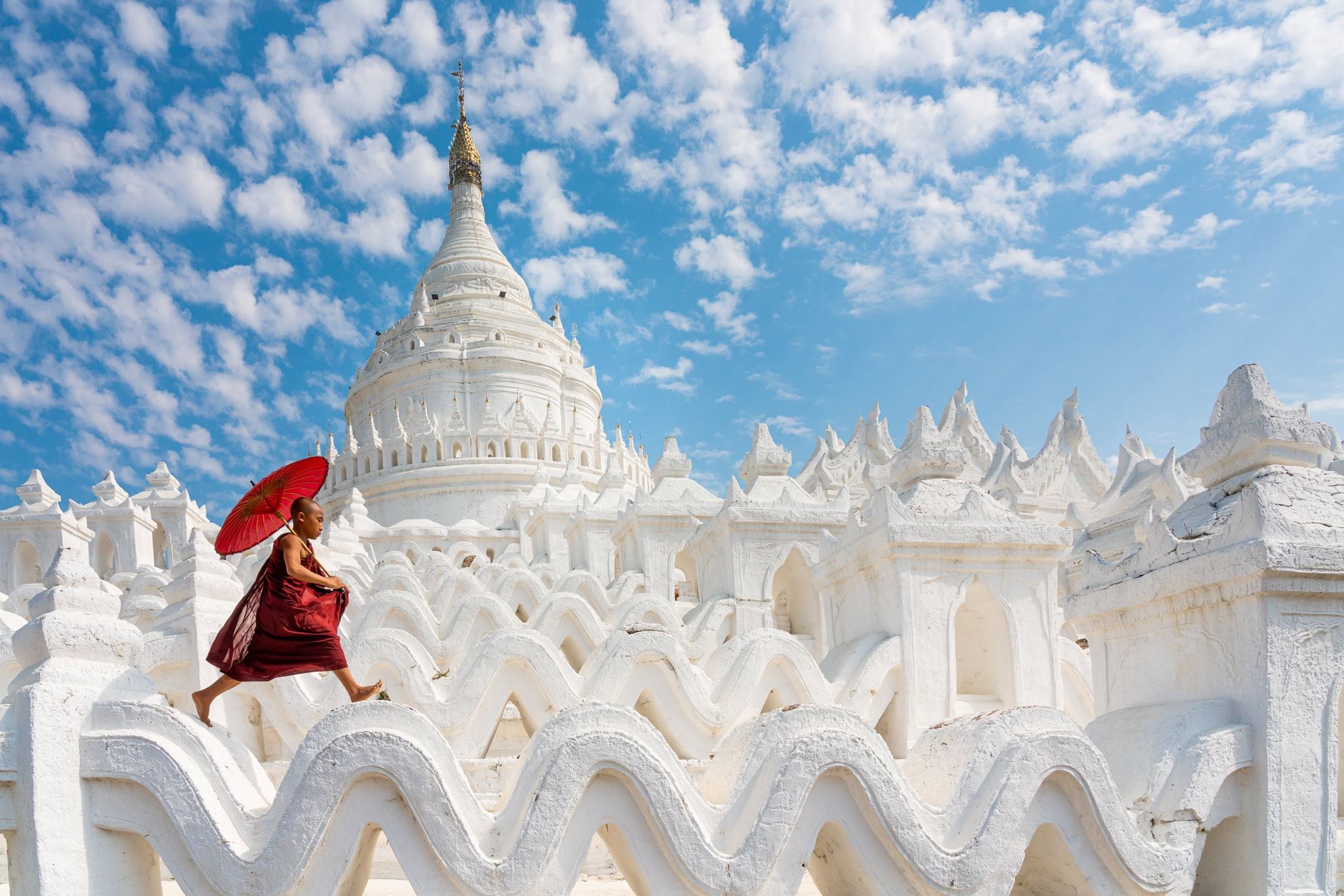 Young Buddhist novice monk jumping on white pagoda structures at Hsinbyume Pagoda, Myanmar
