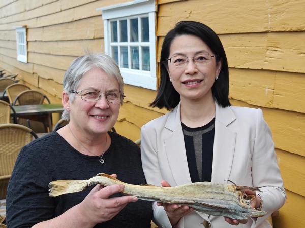 Vertskap og Kinas ambassadør med tørrfisk foran det gule hovedhuset